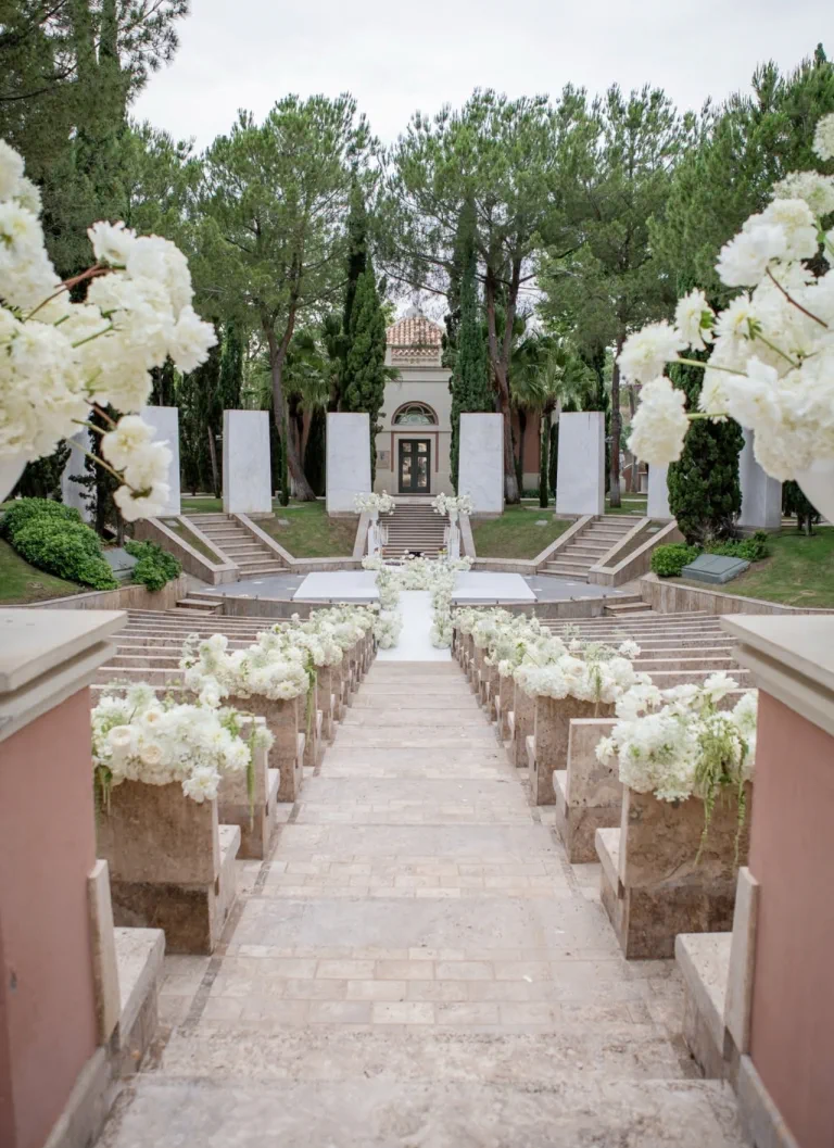 Pasillo de la ceremonia con arreglos de flores blancas sobre pedestales de piedra en el Anantara Villa Padierna