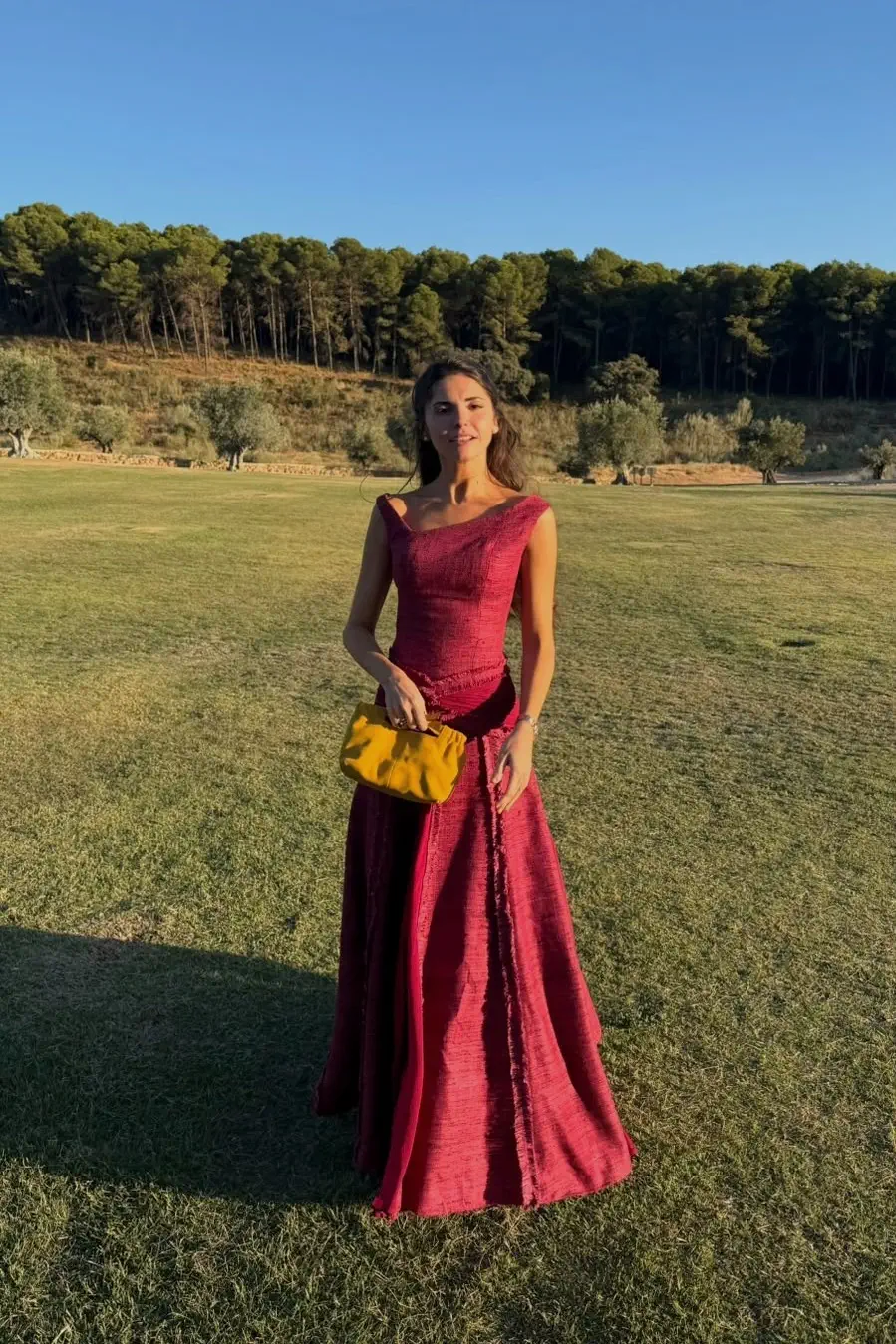 María de cuerpo entero en el césped de Cortijo Curiel, con su vestido granate y un bolso mostaza