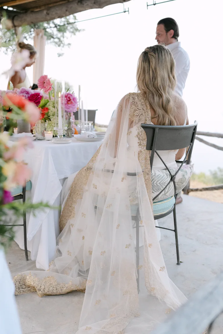 Ashton, con la capa bordada y ondas sueltas, junto a la mesa del porche de Sa Pedrissa entre flores