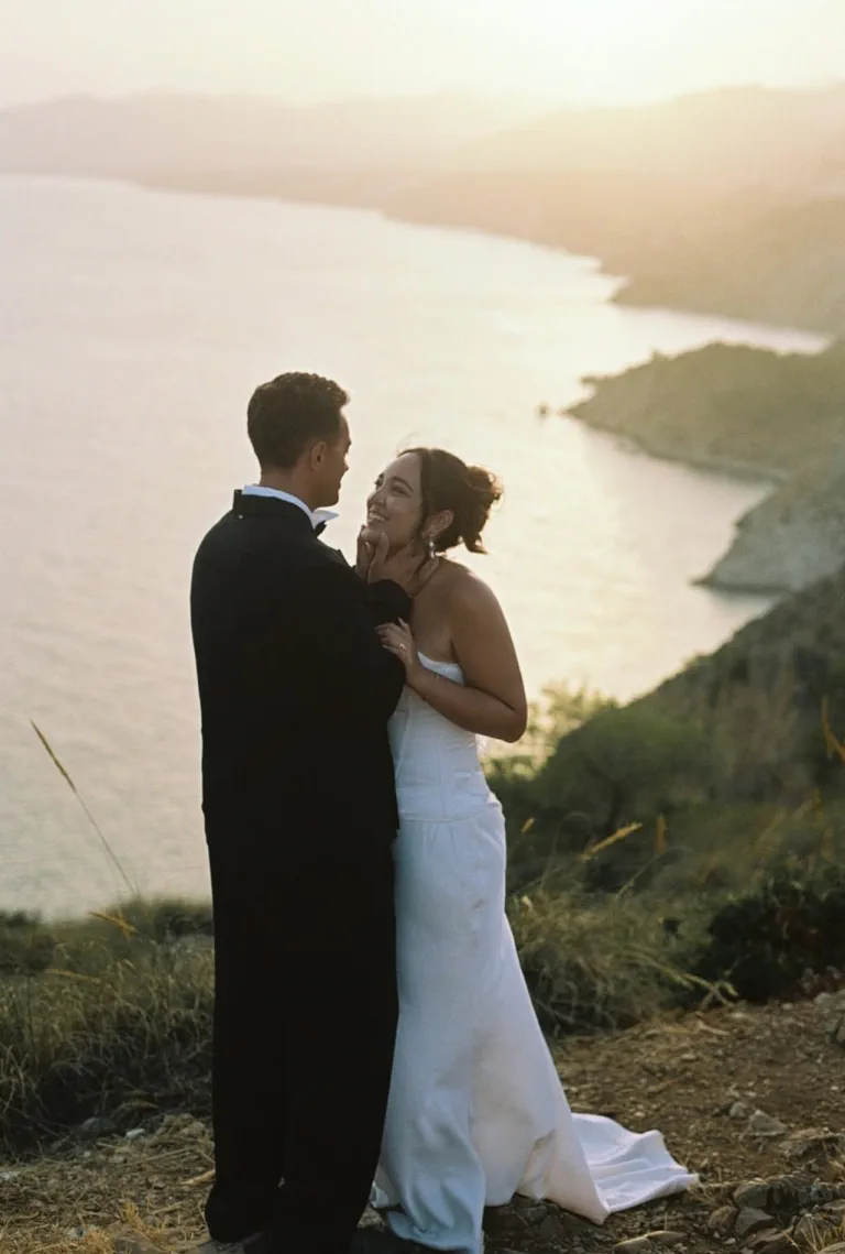 La novia sonríe con su recogido de mechones sueltos, con la bahía al amanecer detrás