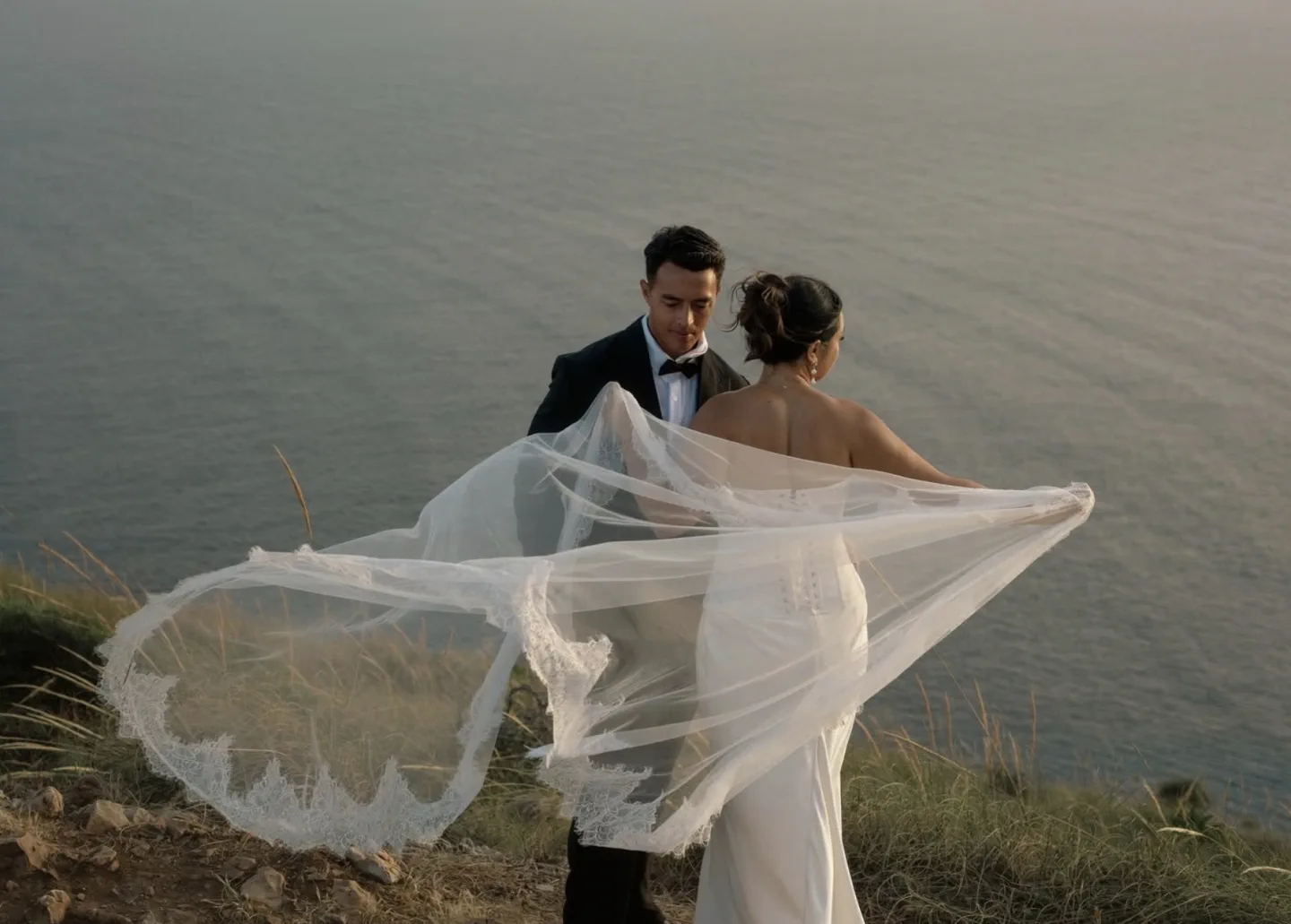 Los novios en lo alto de un acantilado sobre el mar, con el velo al viento, en una elopement en Málaga