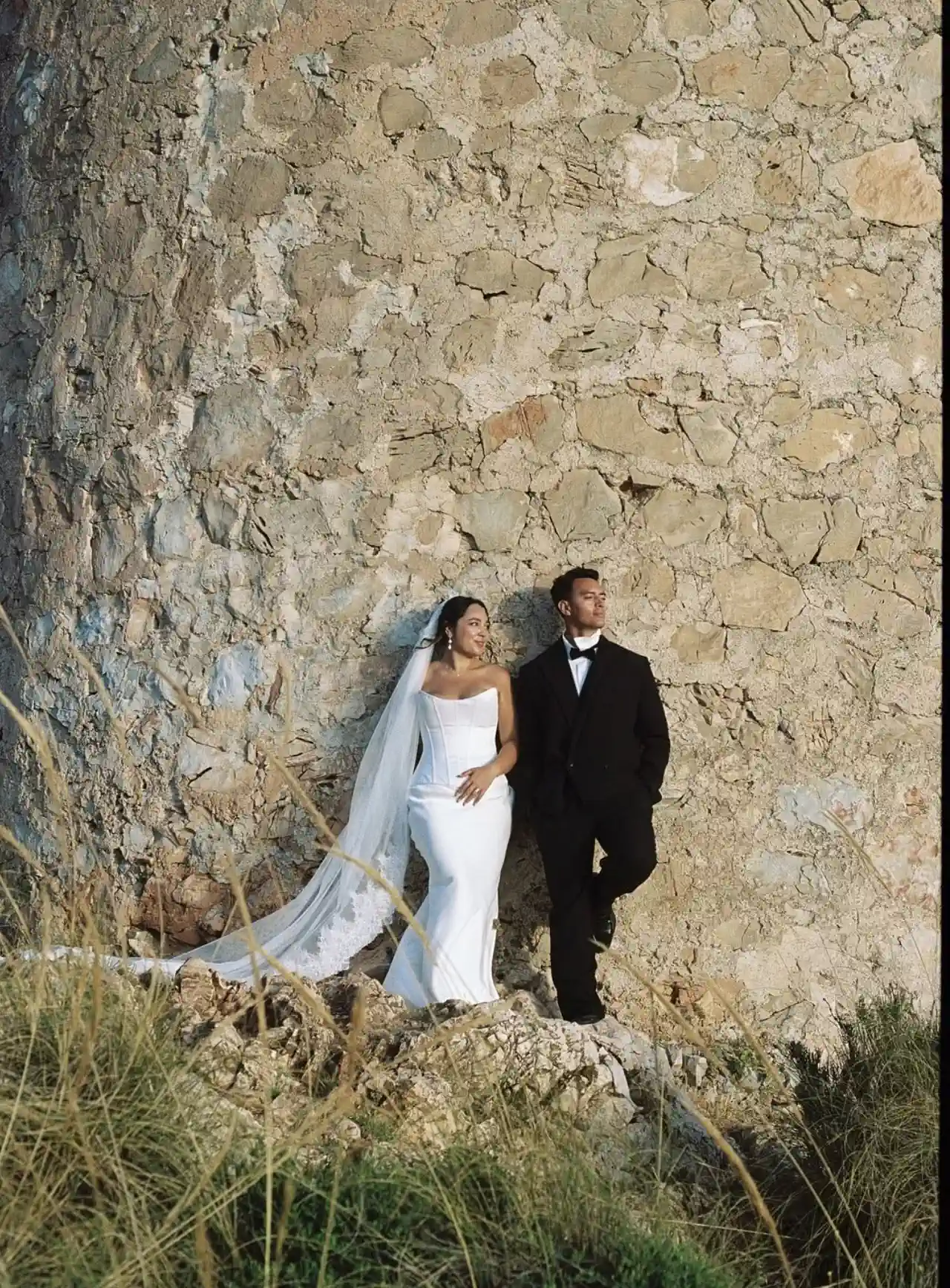La novia, de cuerpo entero y con recogido ondulado, junto a una torre vigía