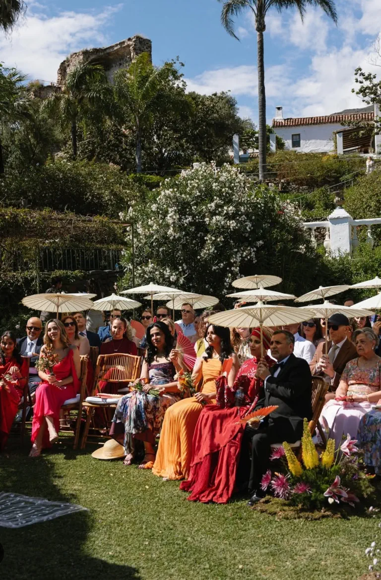 Invitados sentados bajo sombrillas durante la ceremonia en el jardín de Torre de Tramores