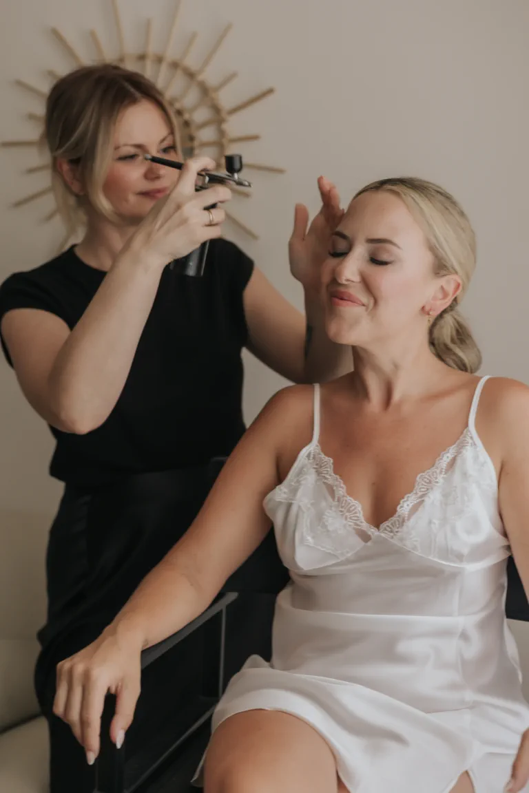 La maquilladora fija el maquillaje luminoso de la novia al final de la preparación de su boda en Mijas