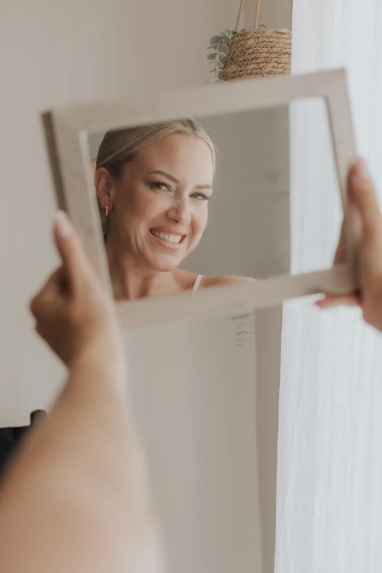 Novia sonriendo ante un espejo de mano con maquillaje soft glam luminoso y colorete rosa