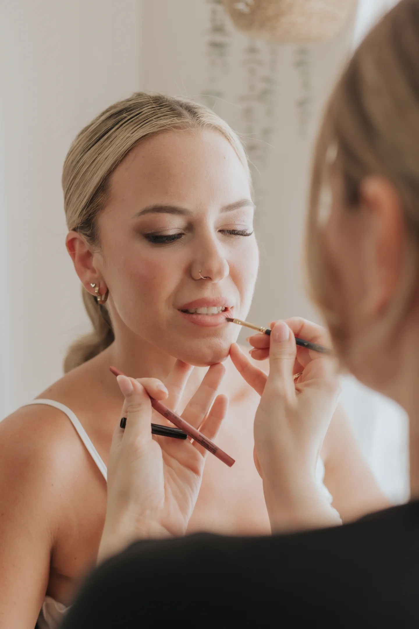 Novia con maquillaje soft glam luminoso mientras la maquilladora le perfila los labios con pincel