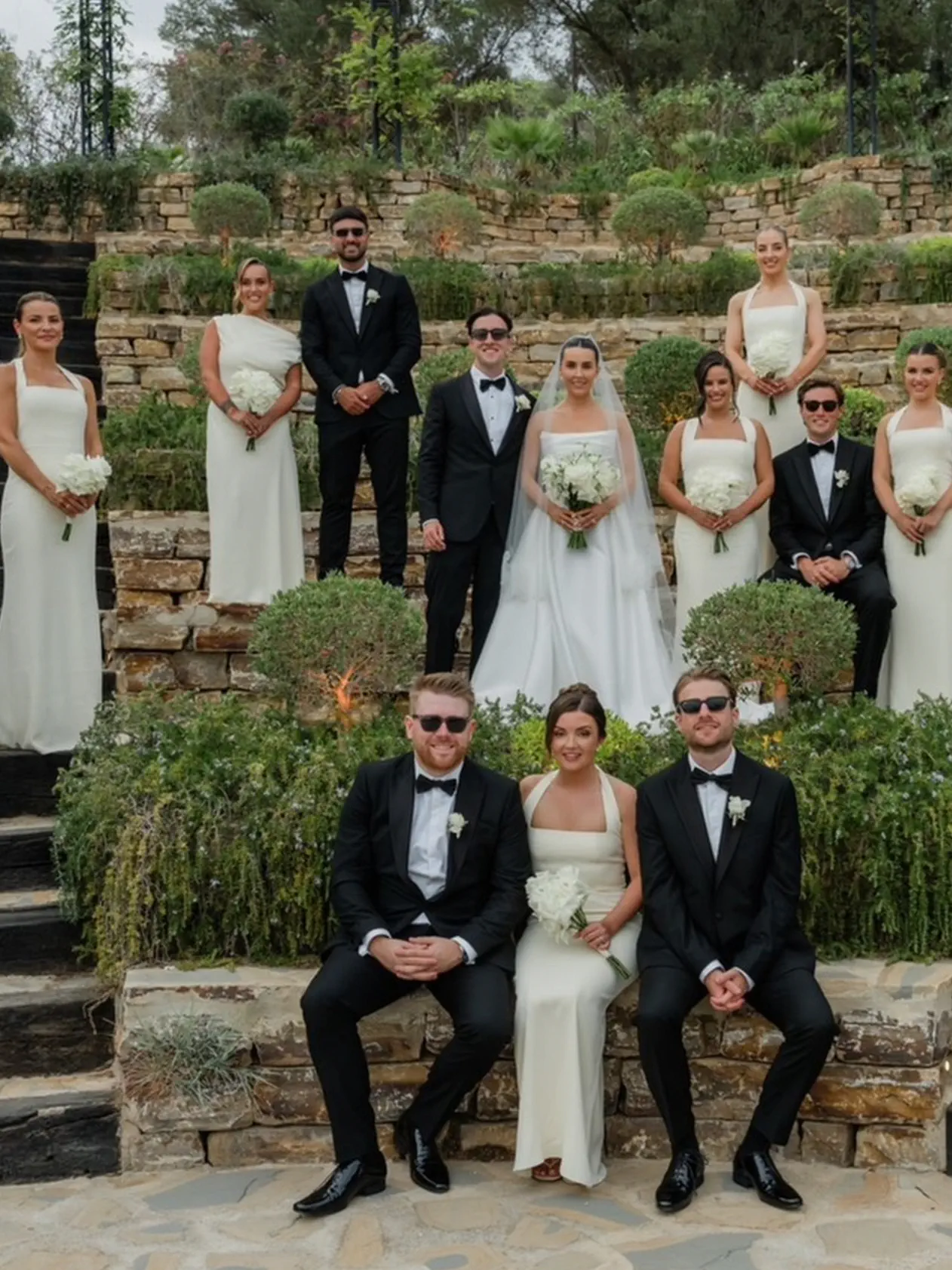 Los novios con las damas de honor y los padrinos en el jardín de terrazas de piedra