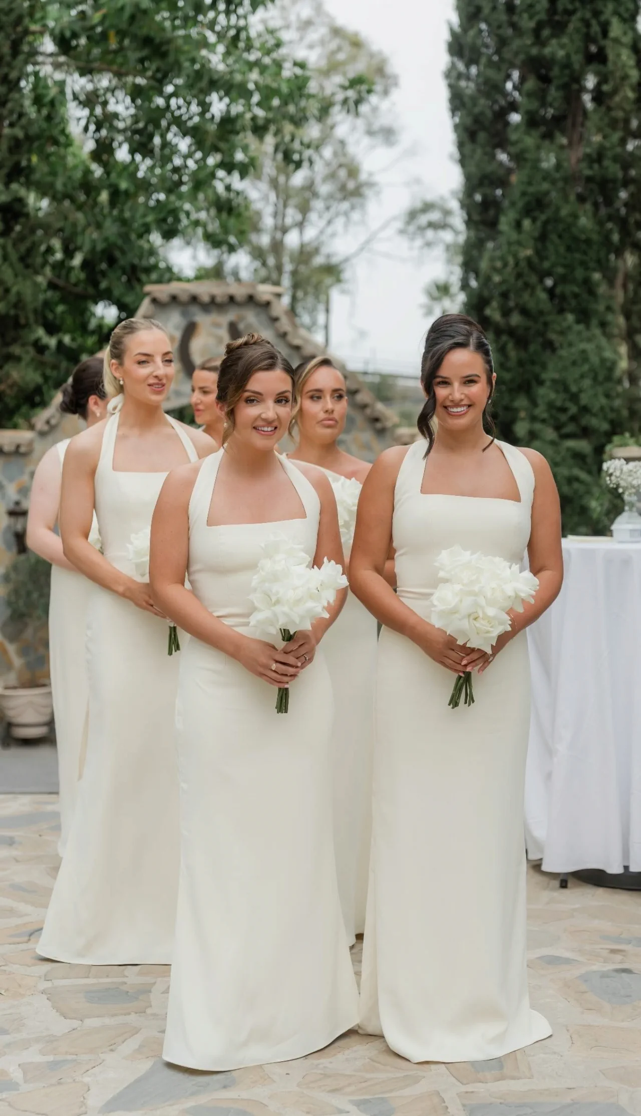 Damas de honor en fila, con vestidos color crema, recogidos pulidos y ramos blancos